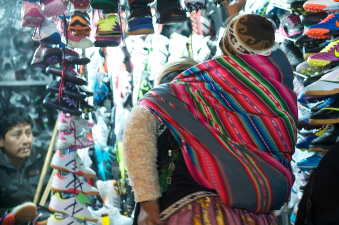 A cholita carries a baby on her back while sifting through goods at night in El Alto. 